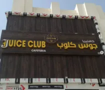 Sign for Juice Club Cafeteria, featuring bold yellow letters against a dark wooden background, with Arabic text included